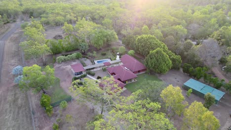 Drone-shot-of-a-sunset-over-a-rural-estate-with-a-large-red-house,-swimming-pool,-pond-and-stone-gardens