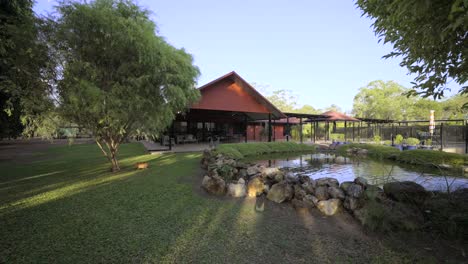 Wide-pull-back-shot-of-a-pond-overlooking-a-large-outdoor-entertainment-area-of-a-red-house