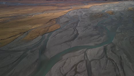 Spectacular-aerial-reveal-over-glacial-river-to-snowy-capped-mountain-range,-winter-landscape-of-New-Zealand