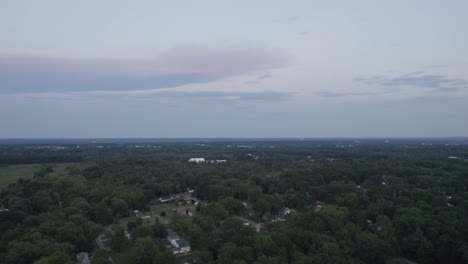 Aerial-drone-forward-moving-shot-over-a-town-surrounded-by-lush-green-vegetation-during-evening-time