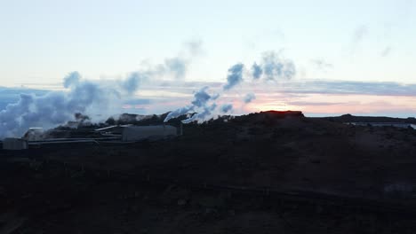 Geothermal-steam-rising-from-electricity-power-plant-in-Iceland-during-sunset,-aerial