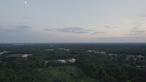 Aerial-drone-shot-hovering-over-a-town-surrounded-by-lush-green-vegetation-during-evening-time-after-sunset
