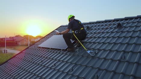 Ingeniero-Revisando-Datos-En-Tableta,-Mientras-Instala-Paneles-Solares-En-El-Techo-De-Una-Casa-Privada---Vista-Aérea