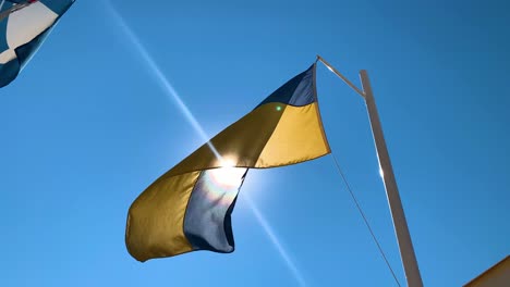 Ukrainische-Flagge-Auf-Einer-Stange,-Die-Gegen-Harte-Sonnenstrahlen-Im-Hintergrund-Flattert