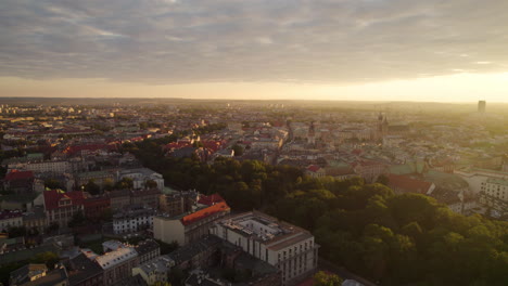 Aerial-backwards-flight-over-lighting-city-of-Krakow-at-golden-sunset-in-Poland,Europe