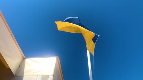 Ukrainische-Flagge-Vom-Wind-Neben-Gebäude-Auf-Klaren,-Blauen-Himmelshintergrund-Geschüttelt