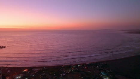Aeriald-dolly-in-of-calm-sea-shore-and-La-Boca-Surf-sand-beach-with-colorful-purple-sunset-in-Concon,-Valparaiso,-Chile