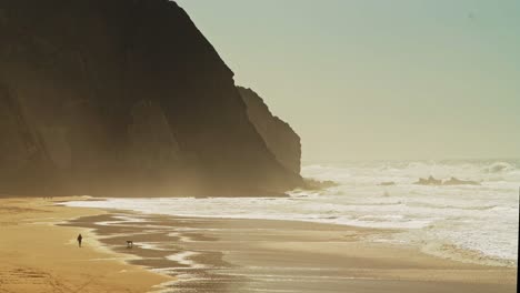 Aerial-Drone-shot-of-People-Walking-The-Dog-on-Praia-Grande-Sandy-Beach-in-Sintra,-Lisbon,-Portugal,-with-Cliffs-and-Beautiful-Coastal-Scenery-Coastline-Landscape