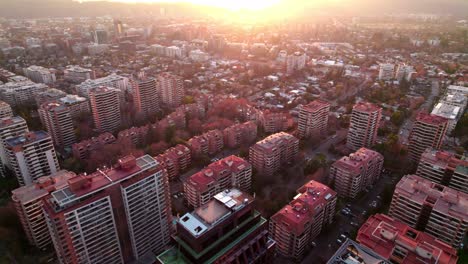 Aerial-dolly-in-of-high-rise-Vitacura-neighborhood-buildings-at-golden-hour-with-sun-beams-in-horizon,-Santiago,-Chile