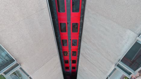 Aerial-tilt-up-of-metal-and-glass-elevator-with-red-and-black-details-in-modern-concrete-building