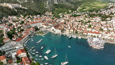 Hvar-Island-drone-footage-capturing-the-boats-entering-the-harbor,-the-town-centre,-surrounding-landscapes,-and-Hvar-Fortress-on-the-hill