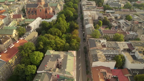 Aerial-flyover-road-with-cars-beside-trees-and-Saints-Peter-and-Paul-Church-in-krakow-during-sunrise