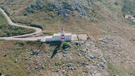 Aerial-drone-rotating-shot-of-a-white-and-red-colored-lighthouse-located-in-Cabo-Silleiro-along-the-mountain-slope-at-daytime