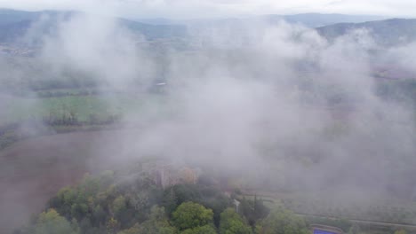 Soaring-through-mist-clouds-revealing-medieval-castle-on-hill-in-Italy