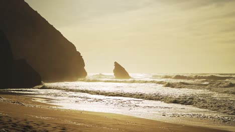 Praia-Da-Adraga-Strand-In-Portugal,-Lissabon-Bei-Wunderschönem-Orangefarbenen-Sonnenaufgang,-Mit-Wellen,-Die-Am-Sandufer-Brechen,-Und-Felsformationen-Auf-Der-Dramatischen-Portugiesischen-Küstenlandschaft-Bei-Sintra,-Europa