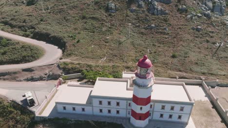 Aerial-drone-shot-of-a-white-and-red-colored-lighthouse,-located-at-cabo-Silleiro,-on-a-hilly-area-at-daytime