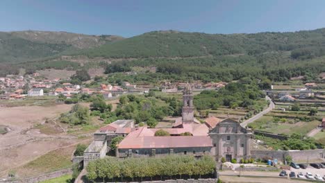 Aerial-drone-forward-moving-shot-over-a-damaged-historic-monastery-called-Santa-Maria-de-Oia-with-bell-tower-on-the-foothills-of-a-mountain-range