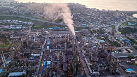 Bird's-eye-view-dolly-in-of-an-oil-refinery-with-smoking-burner,-machinery-in-operation-at-dusk