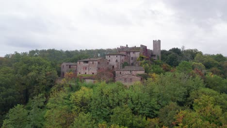 Cultural-brick-Italian-settlement-on-top-of-woodland-hill-overlooking-valley,-aerial