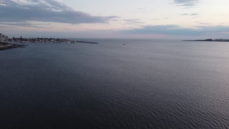 Aerial-flyover-ocean-water-showing-fishing-boat-arriving-harbor-of-Punta-del-Este-in-uruguay-in-the-evening
