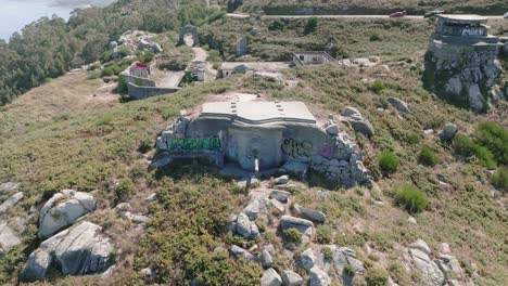 Aerial-drone-backward-moving-shot-of-old-abandoned-army-bunkers-with-cannon-used-in-spanish-civil-war-along-hilly-terrain-along-the-coastline-at-daytime