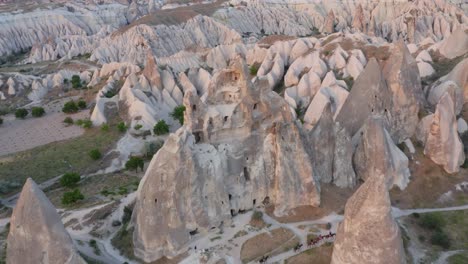 Flying-away-from-rock-formation-church-with-horses-trotting-along-fairy-chimneys-revealing-full-landscape-in-Cappadocia-turkey