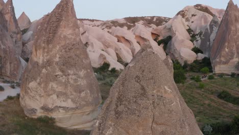 Rotation-around-close-up-of-fairy-chimney-natural-rock-formation-above-grass-fields-to-reveal-landscape-in-Cappadocia-turkey