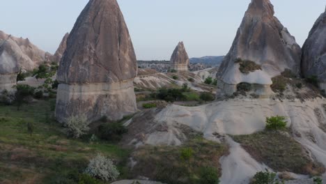 Drone-flying-away-from-close-up-to-medium-of-fairy-tale-rock-formations-in-grass-fields-Cappadocia-turkey