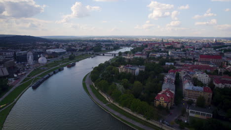Aerial-flyover-Vistula-River-and-historic-city-of-Krakow-in-Poland-with-green-trees-at-river-shore