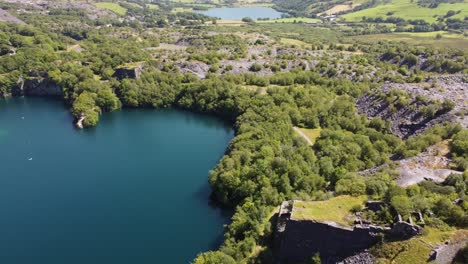Aerial-view-flying-above-Snowdonia-valley-Dorothea-quarry-woodland-tilting-to-turquoise-lake-below