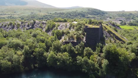 Aerial-view-orbiting-Dorothea-slate-quarry-woodland-with-Snowdonia-mountains-in-the-background