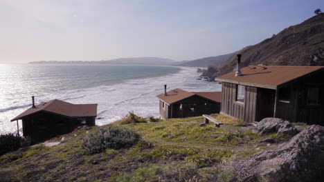A-cluster-of-rustic,-vintage-cabins-overlooking-a-rocky-coastal-shore-at-a-beach-near-San-Francisco,-California