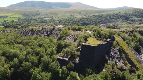 Aerial-view-rising-above-Dorothea-slate-quarry-woodland-with-Snowdonia-mountains-in-the-background