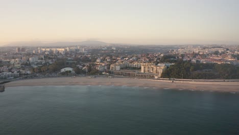 Aerial-view-of-marginal-over-ocean-in-Santo-amaro-beach-of-Oeiras,-sunset-in-Portugal---drone-shot-In-Silhouette-Mood