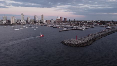 Aerial-view-of-fishing-boat-arriving-harbor-of-Punta-del-Este-with-skyline-in-background-at-dusk---Uruguay,South-America