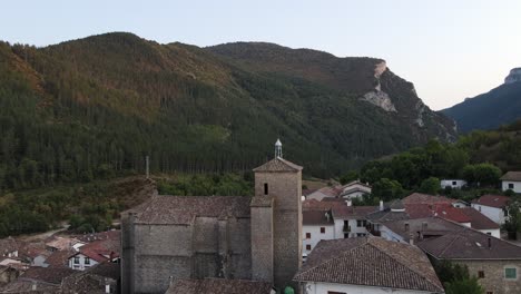 Drone-take-off-from-field-in-Burgui,-Spain-rises-above-village-reveals-wide-mountain-landscape
