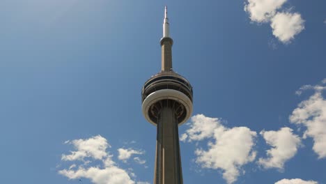 Rotating-drone-video-of-the-top-of-CN-Tower-against-the-clouds-with-helicopter-flying-by-in-Toronto-Ontario-Canada