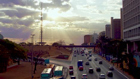 Typical-city-traffic-in-Brasilia,-Brazil-at-sunset-with-sunbeams-shinning-through-the-clouds
