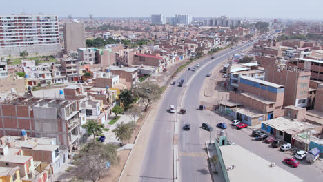 Zoom-in-shot-with-drone-of-the-famous-Peruvian-highway-"Panamericana-Norte"-in-the-city-of-Chiclayo-while-cars-and-trucks-travel-with-houses-and-buildings-in-the-background-in-the-morning