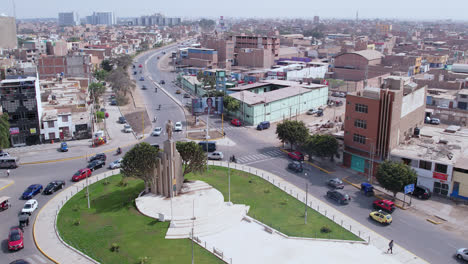Amazing-drone-shot-over-the-famous-"Ovalo-QuiÃ±ones"-oval-with-a-statue-on-the-highway-of-the-city-of-Chiclayo,-Peru-while-cars-drive-around-during-the-day