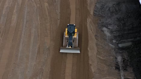 Drohnenschuss-Nach-Gelbem-Bulldozer,-Der-Durch-Abgestuften-Sand-Rückwärts-Fährt-Und-Spuren-Hinterlässt