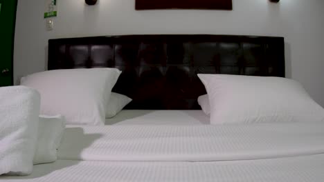 Empty-Hotel-Room,-black-and-white-bed,-pillowa-and-towels,-close-up-Pan-right