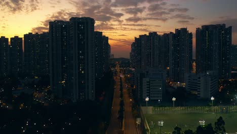 Drone-shot-traveling-forward-above-a-busy-street-in-an-urban-area-full-of-public-housings-buildings-during-sunset