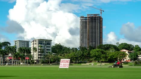 Albert-Park-in-Suva-city-with-tall-skyscraper-under-construction,-cumulus-clouds,-ground-closed-sign,-timelapse