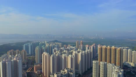 Toma-Cinematográfica-De-Un-Dron-Que-Viaja-Hacia-Atrás-Sobre-Un-Suburbio-De-Hong-Kong-Durante-El-Día,-La-Ciudad-Distante-Shenzen-Es-Visible