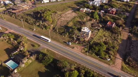Aerial-tracking-shot-of-tour-bus-driving-on-main-road-iof-Punta-del-Este-at-sunset-light