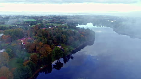 Flying-through-clouds-over-a-reflective-lake-and-a-village-in-Europe-in-Autumn
