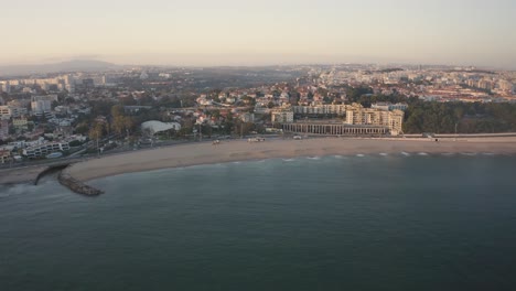 Aerial-drone-view-overlooking-the-Santo-Amaro-beach-cityscape,-sunset-sky-horizon-in-Lisbon