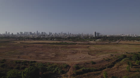 Aerial-slide-to-the-left-over-uncultivated-agricultural-land,-the-city-of-Tel-Aviv-in-the-distance