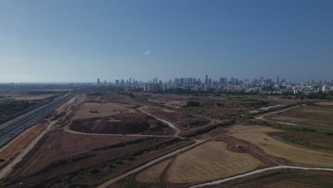 Aerial-quick-slide-to-the-right-over-a-main-road,-agricultural-fields-and-the-city-of-Tel-Aviv-in-the-distance